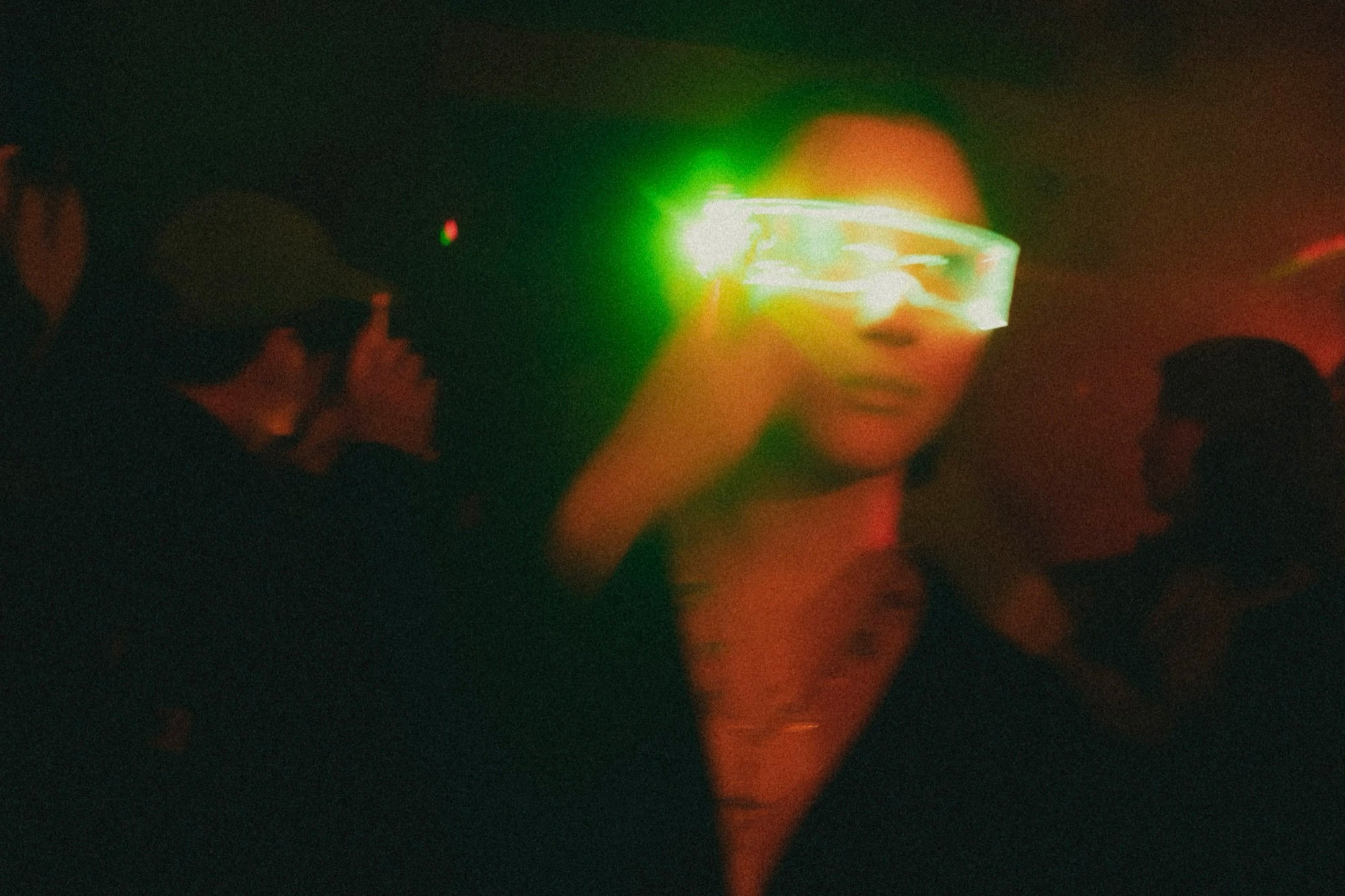 A dancer in glowing LED visor glasses on a dark, green-lit floor at an A.S.F. night